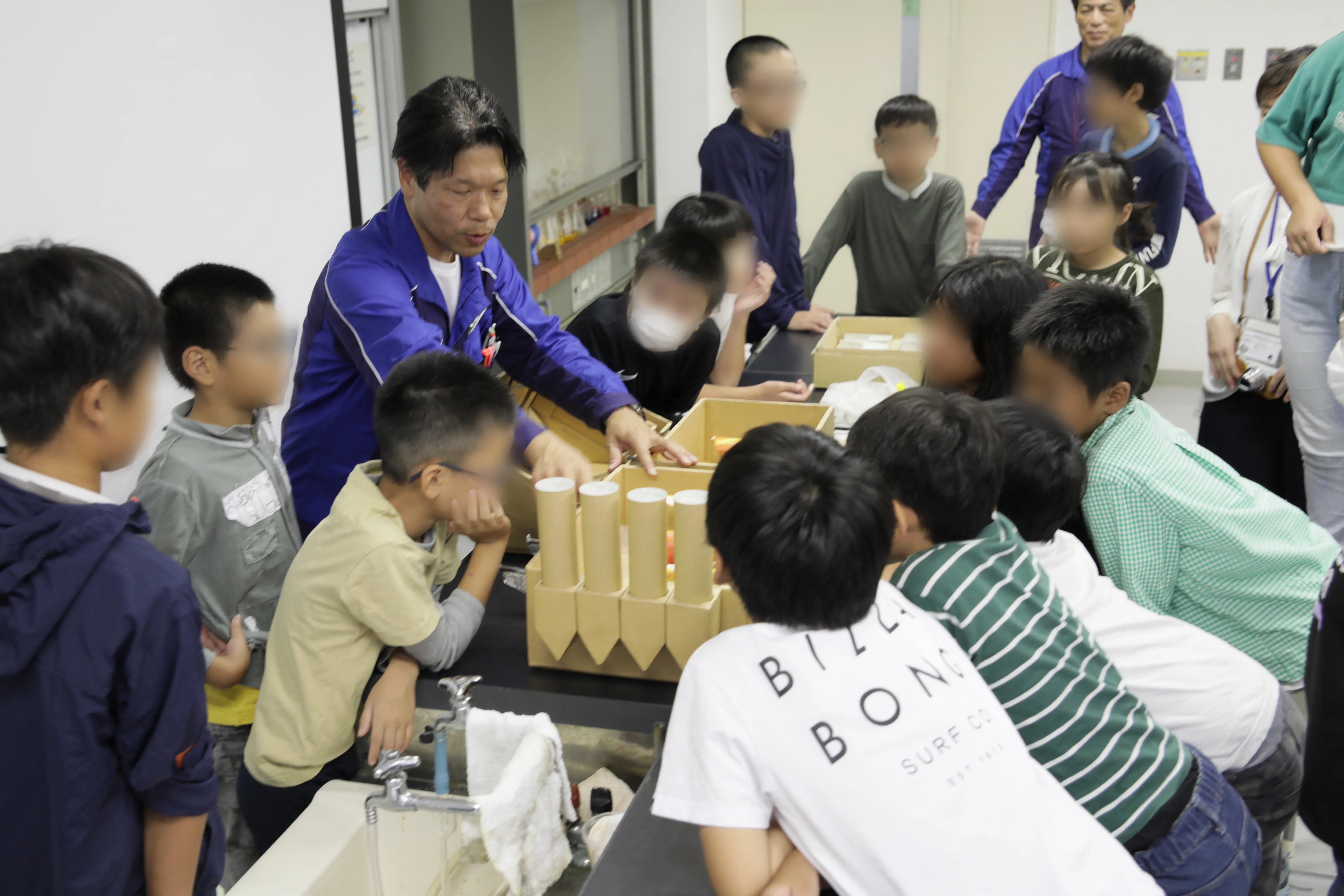 ガラス溶融炉の模型とそれを囲って観察する子どもたち